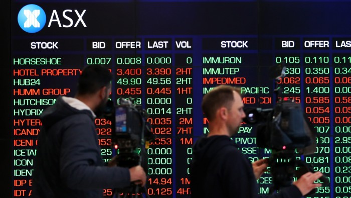 People walk past an Australian Securities Exchange electronic board