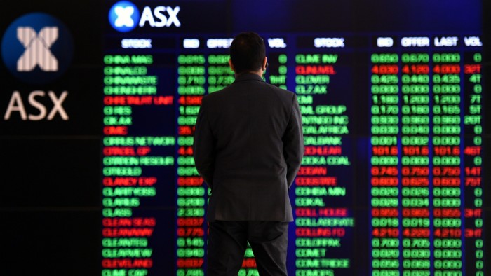 A man stands in front of an electronic trading board at the Australian Stock Exchange