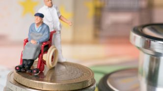 Figures of aged carer and man in wheelchair on top of coins