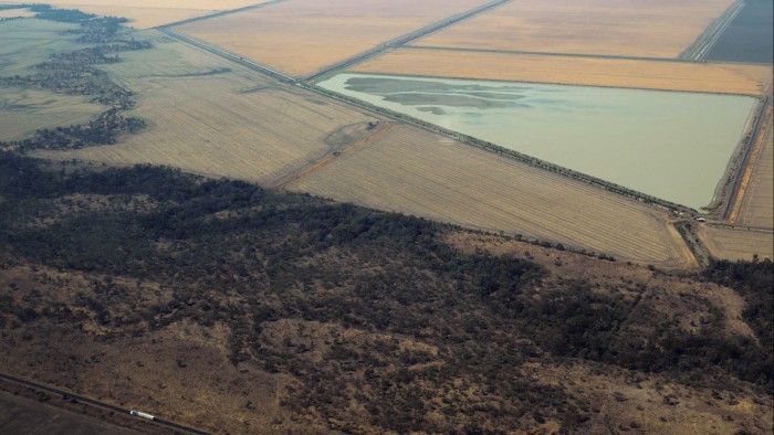 Aerial view of a vast rural landscape with agricultural fields, a reservoir, and patches of dry woodland, intersected by roads stretching across the terrain